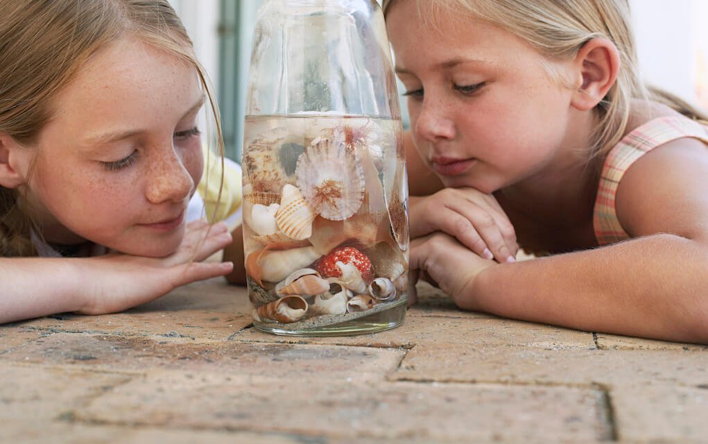 Two girls looking at shells in a jar for beach craft ideas