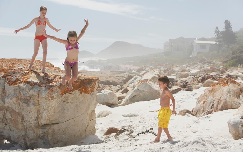 Children climbing a big rock at the beach