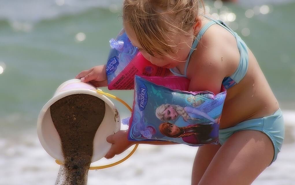 Little girl pouring sand on the beach